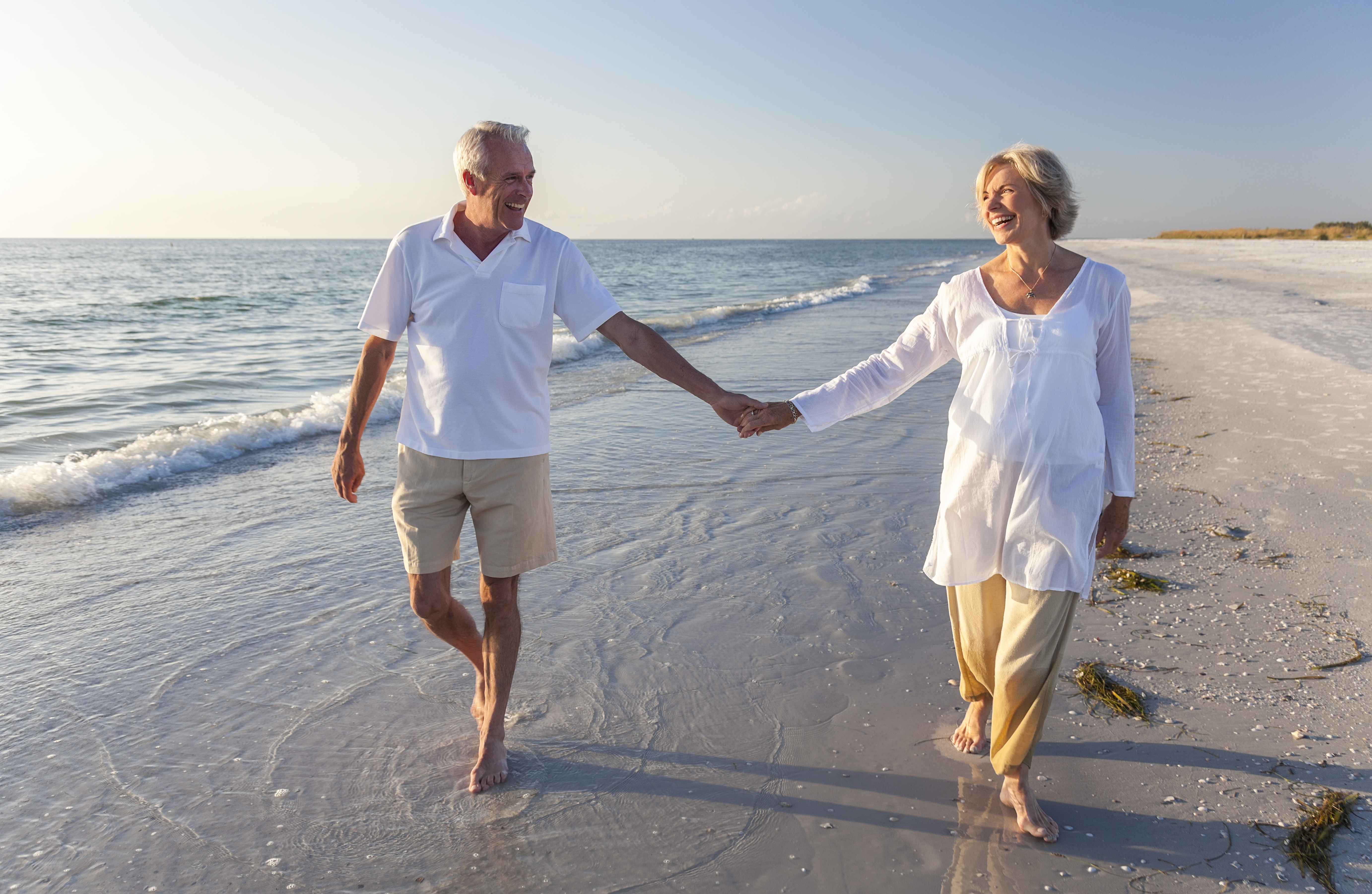 Happy senior man and woman couple walking and holding hands on a deserted tropical beach with bright clear blue sky