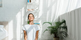 beautiful happy girl with closed eyes practicing yoga in lotus position in bedroom in the morning