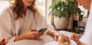 Woman using mobile phone during manicure at spa