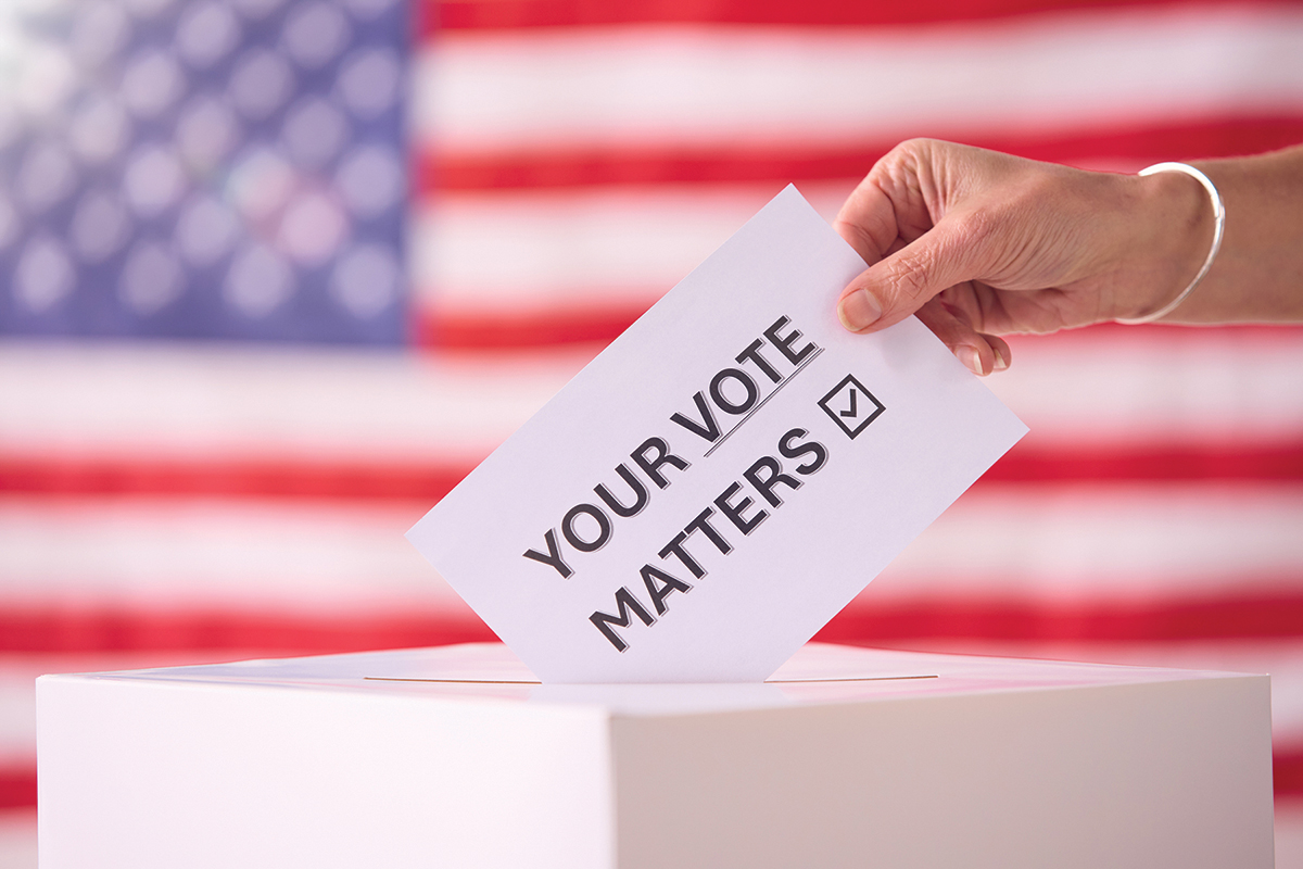 Hand Placing Ballot in Box With American Flag