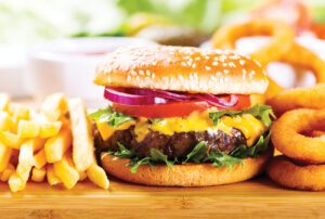 hamburger with fries and onion rings on wooden table