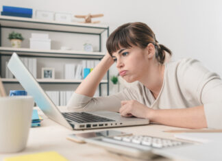 Tired disappointed woman working at office desk with a laptop, connection and computer problems concept