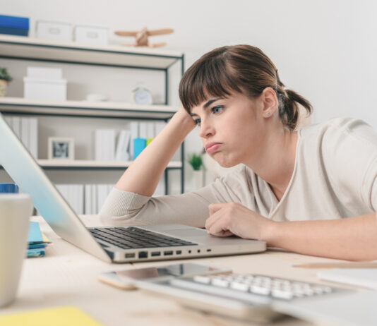 Tired disappointed woman working at office desk with a laptop, connection and computer problems concept