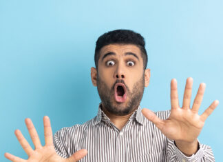 Shocked bearded businessman screaming in horror and fear, keeping hands raised to defend himself.