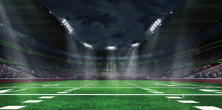 American football arena with yellow goal post, grass field and blurred fans at playground view. 3D render. Flashlights