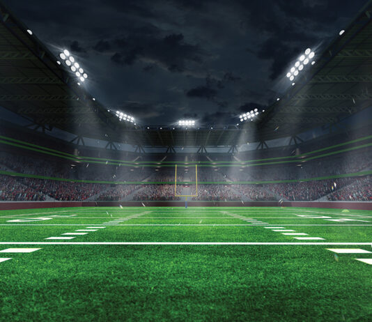 American football arena with yellow goal post, grass field and blurred fans at playground view. 3D render. Flashlights