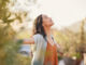 Young latin woman with arms outstretched breathing in fresh air during sunrise at the balcony. Healthy girl enjoying nature while meditating during morning with open arms and closed eyes. Mindful woman enjoying morning ritual while relaxing in outdoor park.