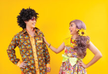 Asian hippie couple dress in 80s colorful vintage fashion with retro clothing while dancing together isolated on yellow background for fancy outfit party and pop culture