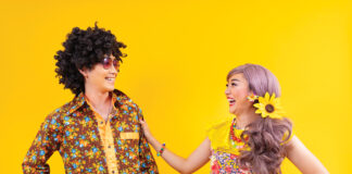 Asian hippie couple dress in 80s colorful vintage fashion with retro clothing while dancing together isolated on yellow background for fancy outfit party and pop culture