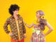 Asian hippie couple dress in 80s colorful vintage fashion with retro clothing while dancing together isolated on yellow background for fancy outfit party and pop culture