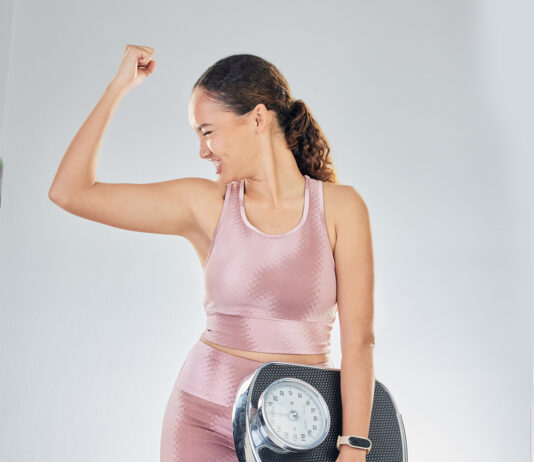 Scale, success and strong woman with fitness, lose weight progress and body goals or fist, power and bodybuilder. Sports person or model for achievement, diet and yes sign on studio, white background